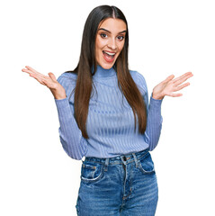 Young beautiful woman wearing casual winter sweater celebrating victory with happy smile and winner expression with raised hands