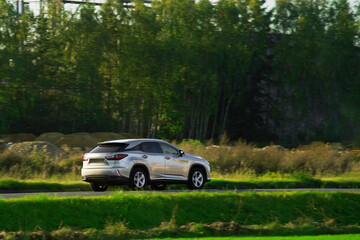 Speeding on a road in a sporty luxury car with a sunset and forest background. Sophisticated...