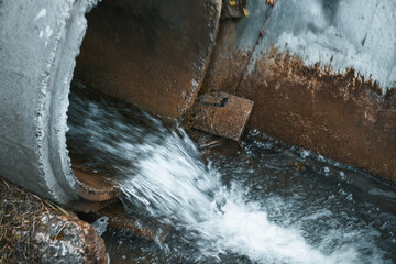 The river is polluted by industrial waste from a drainpipe that dumps sewage into the water, harming the natural ecosystem.