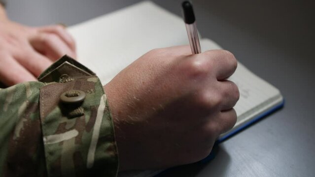 Unrecognizable army soldier marine writing in a book or diary with a pen close up on hand