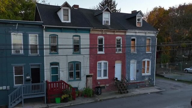 Colorful row houses with gabled roofs at dusk. Boarded up and abandoned home in crime-ridden, dangerous neighborhood in USA city. Aerial.