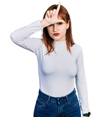Fototapeta premium Redhead young woman wearing casual turtleneck sweater making fun of people with fingers on forehead doing loser gesture mocking and insulting.