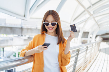 Happy Asian girl standing using smartphone and holding credit card with enjoys freedom.