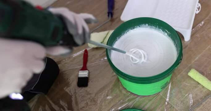 The builder in the room mixes the paint in a bucket with a whisk, repairs. White paint for the wall