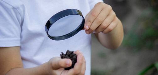 The child examines the ground with a magnifying glass. Selective focus.