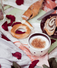 Breakfast in bed close-up, cappuccino in a light cup and pastries with poppy seeds on a board, against the background of a kitchen towel, a red rose and blanket
