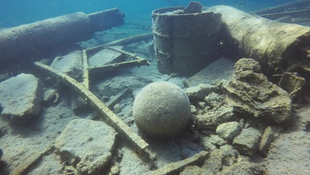 Close-up, Old stone cannonball lying on rocky sea bottom next to destroyed pier in Mediterranean Sea, Greece, Camera moving forwards approaching the cannon ball
