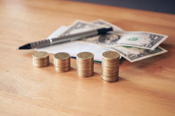 Stack of golden money coin on wood desk with dollar banknote and pen. Business and financial concept. 
