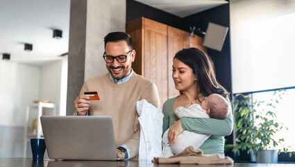 Young family, parents with baby shopping online on laptop with credit card at home. Online shopping - Powered by Adobe