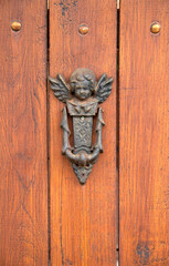 Old knocker in the shape of angel on wooden door closeup