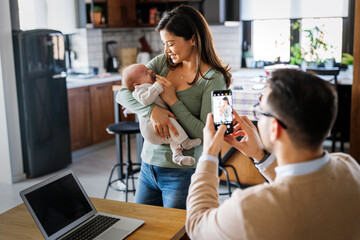 Proud father take picture of his wife with infant baby at home. Happy family, technology concept. - obrazy, fototapety, plakaty