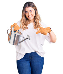 Young caucasian woman wearing gloves holding watering can smiling happy pointing with hand and finger
