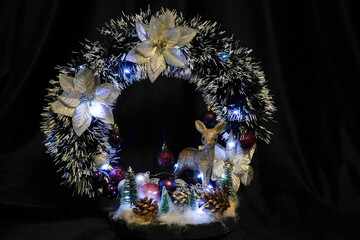 Christmas wreath in the form of a star Blue lights. Symbolic Christmas balls and ornaments. Green, white. On a black background