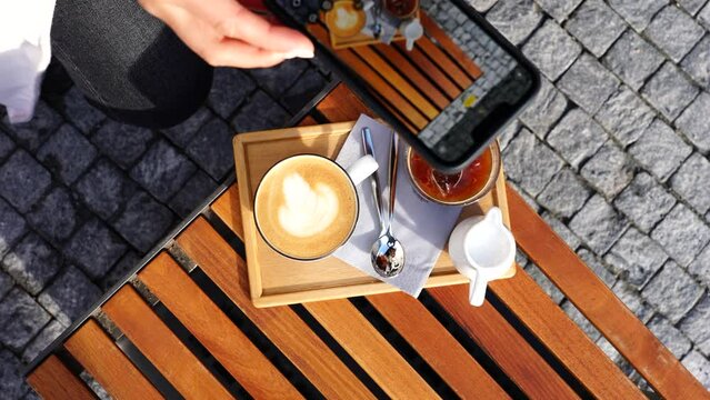 Girl capture multiple photos of latte foam art on wooden outdoor table