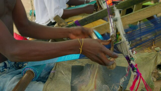Ghanaian man making Kente handwoven cloth with looms rustic equipment. Close up