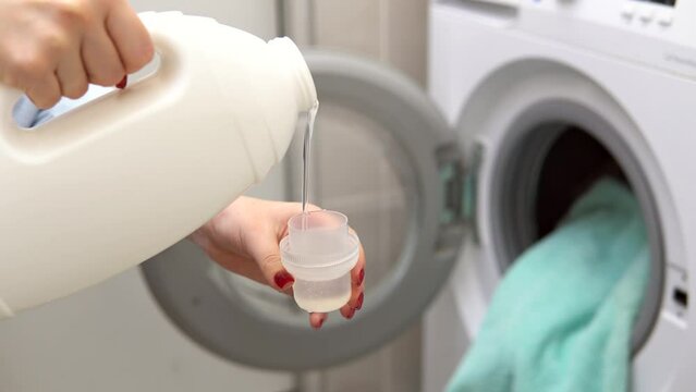 Woman pouring liquid washing gel softener from bottle into cap for washing clothes, closeup.