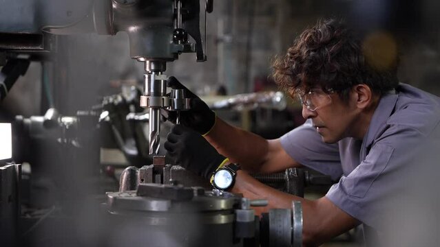 Asian worker in production plant drilling at machine. Professional worker near drilling machine on factory. finishing metal working internal steel surface on lathe grinder machine with flying sparks.