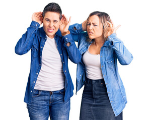 Fototapeta premium Couple of women wearing casual clothes trying to hear both hands on ear gesture, curious for gossip. hearing problem, deaf