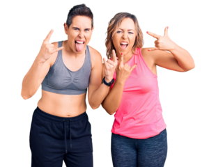 Couple of women wearing sportswear shouting with crazy expression doing rock symbol with hands up. music star. heavy music concept.