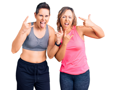 Couple of women wearing sportswear shouting with crazy expression doing rock symbol with hands up. music star. heavy music concept.