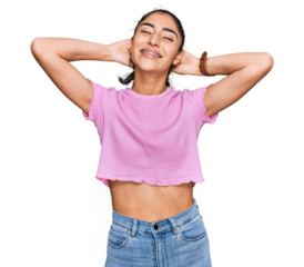 Hispanic teenager girl with dental braces wearing casual clothes relaxing and stretching, arms and hands behind head and neck smiling happy
