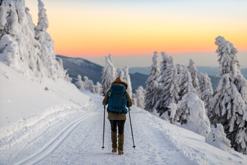 Woman hiking in snow on trekking trail at winter mountains during sunset. Sports and outdoors...