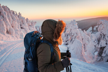 Hiking in winter mountains during sunset. Woman with backpack wearing winter coat with hood. Sports...