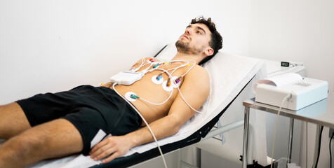 A young man undergoes an electrocardiogram test to diagnose heart disease in a hospital ward....