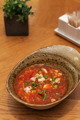 Fresh spicy tomato soup with chicken, green onions, chili peppers and herbs in a restaurant, Asian cuisine. Tom yum soup with chicken. Vertical orientation, hard light.