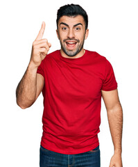Naklejka premium Hispanic man with beard wearing casual red t shirt pointing finger up with successful idea. exited and happy. number one.