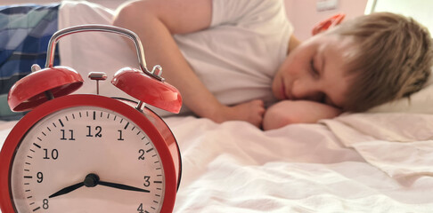 Cute baby sleeps peacefully with an alarm clock in bed