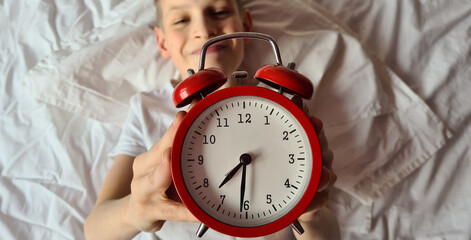 Smiling boy with an alarm clock in bed