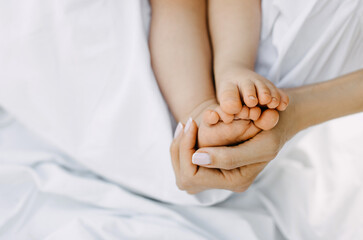 Closeup of mothers hand holding baby barefoot feet.