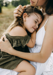 Mother holding her little daughter in arms, comforting and stoking her head, outdoors.
