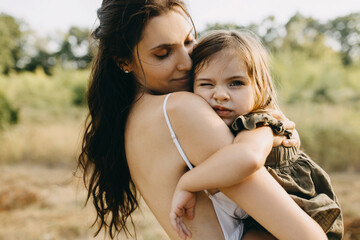 Fototapeta premium Closeup portrait of a mother holding her little daughter in arms, outdoors.
