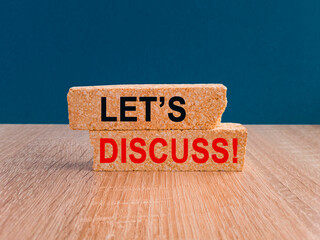 Concept red word LET'S DISCUSS on brick blocks. Beautiful wooden table, blue background. Business concept. Copy space.