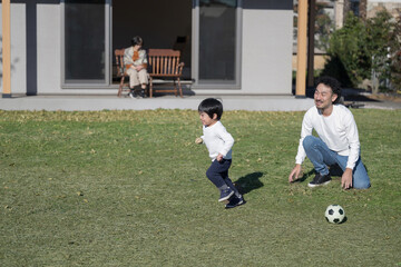 庭で父親とサッカーをする子供と見守る祖母