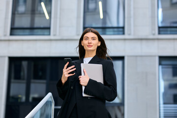 Modern professional in a stylish suit using her phone and laptop to stay productive no matter where she is