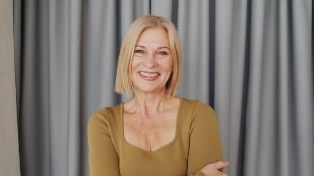 Horizontal medium close-up portrait of beautiful mature woman with blond bob cut hair wearing khaki green clothes smiling at camera
