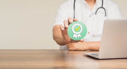 Doctor holding a quality assurance symbol while sitting at a desk.