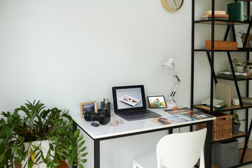 Laptop, digital camera and printed photos on desk of photographer