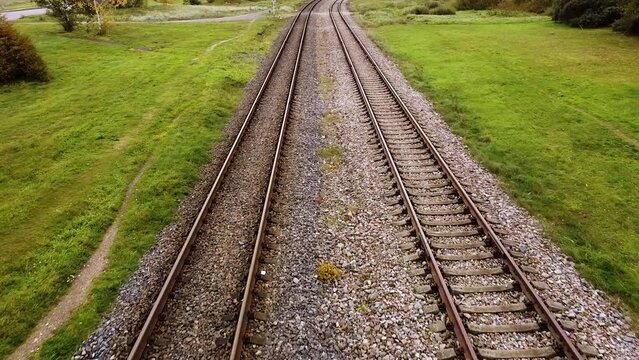 Aerial forward of two old rubble train tracks with grass and tree aside