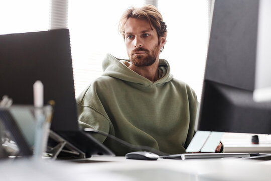 Front view portrait of bearded software developer working on IT project using multiple computer devices