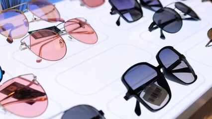 Close-up womans hand taking sunglasses from store window. Window displays dozens of models glasses in frames of different shapes and colors. Stylish showcase delights visitors and inspires purchases.