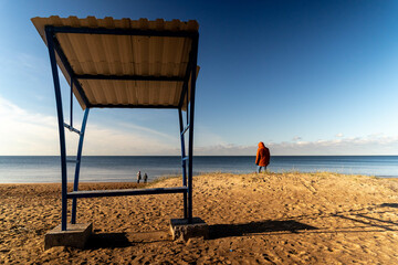 man in a bright hooded jacket strolls along a deserted autumn beach on a sunny day