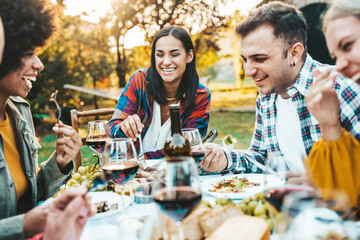 Happy friends having bbq dinner party in garden restaurant - Multiracial young people eating grill meat and drinking red wine in backyard - Food life style concept with guys and girls sitting outdoors - obrazy, fototapety, plakaty