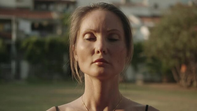 One European female qigong master practicing Chinese breathing exercises with closed eyes outdoors. Close-up. Taoist spiritual and meditation practices. T'ai chi. Image visualization. Zen. 