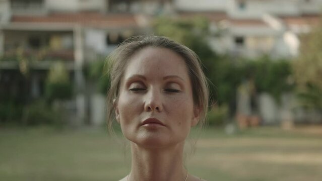 European female qigong master practicing asian breathing exercises with closed eyes outdoors. Close-up. Chinese spiritual and meditation practices. Concentrated attention. Zen. Tai chi. 