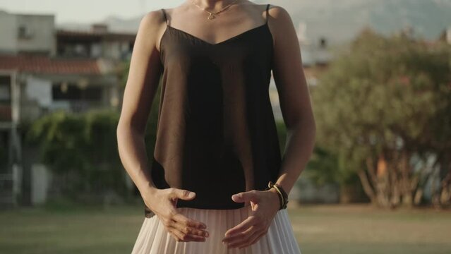 White woman in a black sleeveless tank top practices body position control with her eyes closed in the city park. System of breathing and movement exercises . Qigong. TaiJi. Static training.