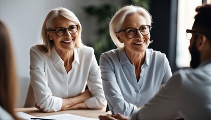 Smiling aged businesswoman in glasses looking at colleague at team meeting, happy attentive female - Powered by Adobe